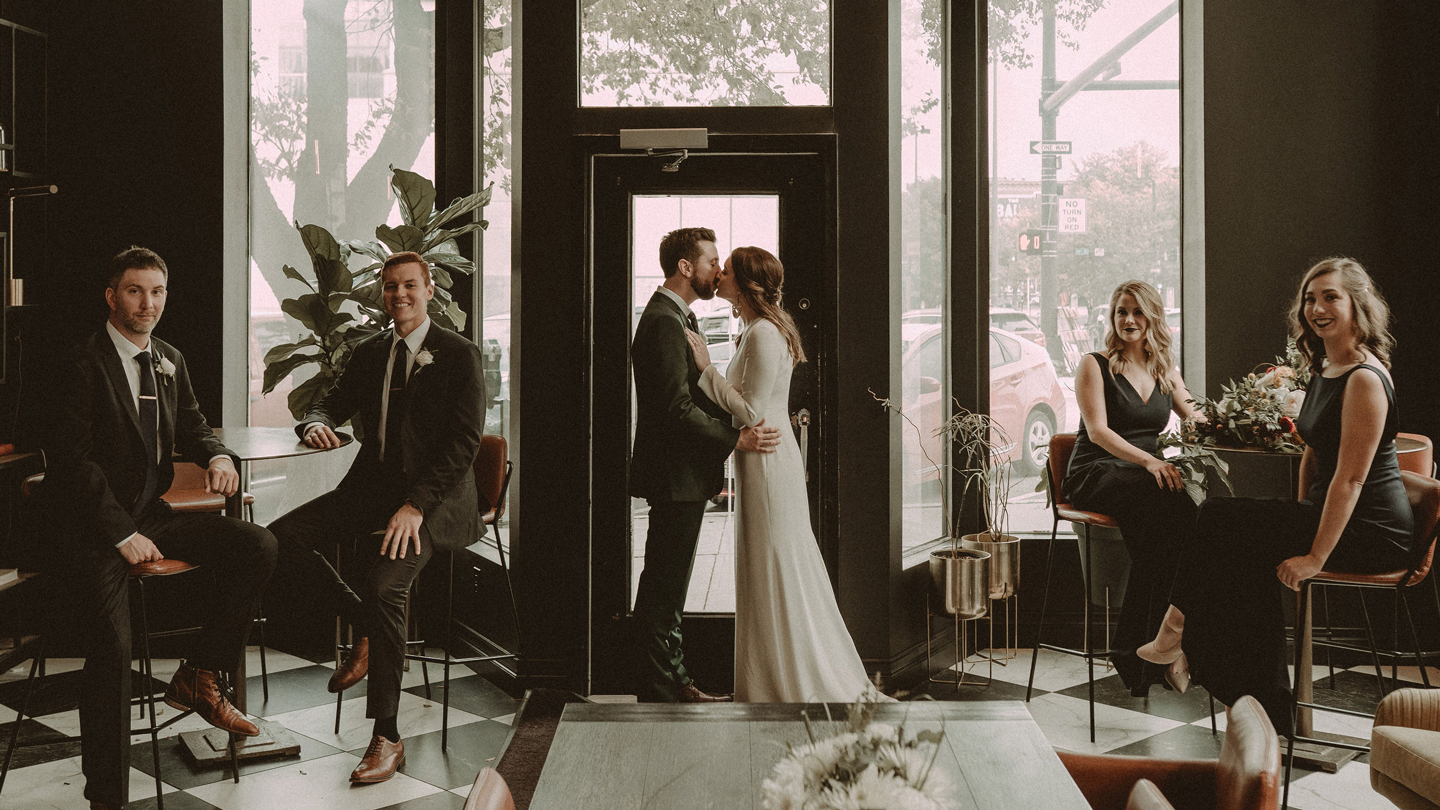 Bride and groom silhouetted in Hotel Deco's grand entrance with floral arch and natural window light