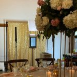 Elegant wedding reception table with tall floral centerpiece, gold sequin backdrop, and candles