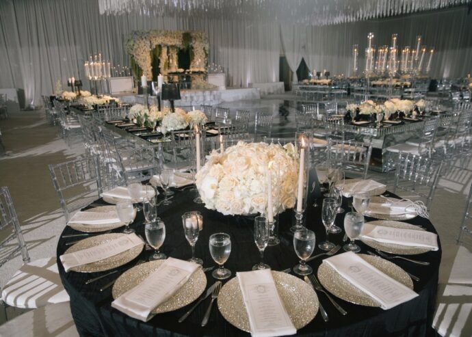 Luxurious reception with black tablecloths, white floral centerpieces, gold chargers, and crystal candelabras throughout ballroom