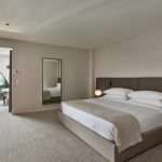 Contemporary hotel suite with king bed, full-length mirror, and terrace overlooking city