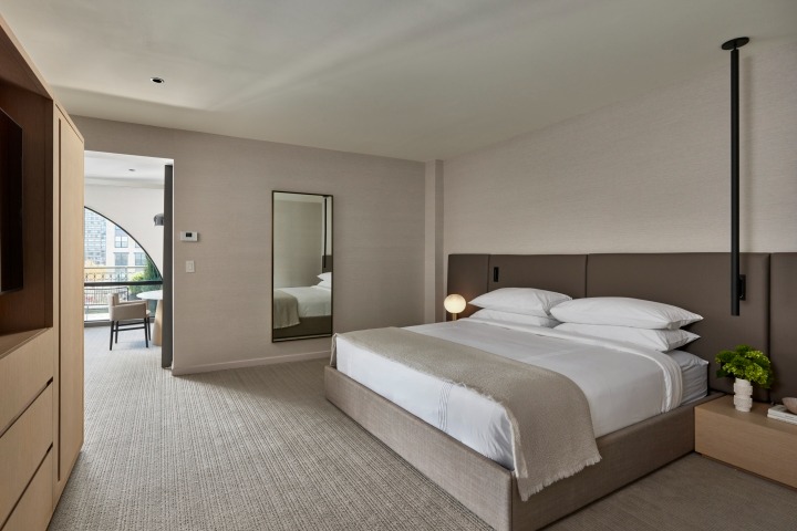 Contemporary hotel suite with king bed, full-length mirror, and terrace overlooking city
