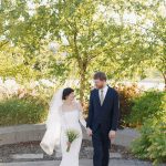 Bride and groom smiling at each other while holding hands outdoors with baby's breath bouquet