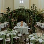 Chapel wedding reception featuring dramatic floral arch over head table, sage linens, and chiavari chairs