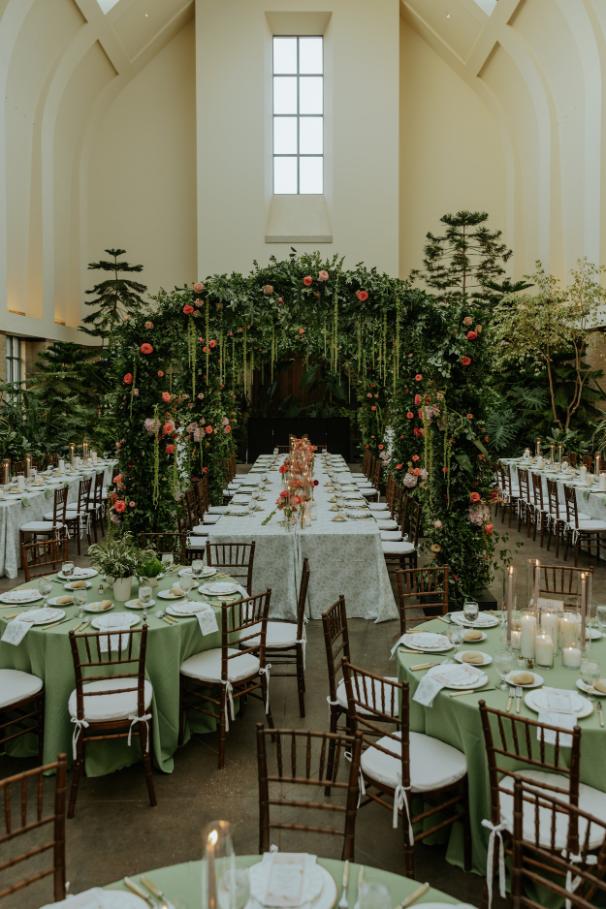 Chapel wedding reception featuring dramatic floral arch over head table, sage linens, and chiavari chairs