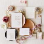 Elegant wedding stationery flatlay featuring blush invitation suite, rings, dried flowers, and silk ribbons