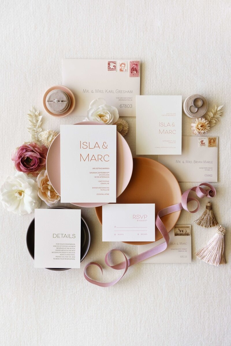Elegant wedding stationery flatlay featuring blush invitation suite, rings, dried flowers, and silk ribbons