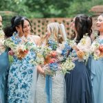 Bridesmaids in blue dresses holding colorful bouquets with ranunculus, dahlias, and delphinium
