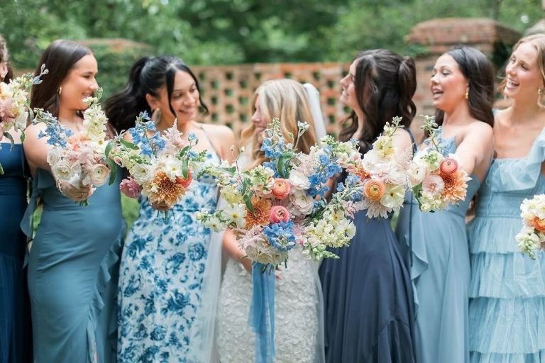 Bridesmaids in blue dresses holding colorful bouquets with ranunculus, dahlias, and delphinium