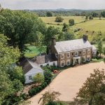 Aerial view of historic stone estate with white tent surrounded by rolling Virginia countryside and mountains
