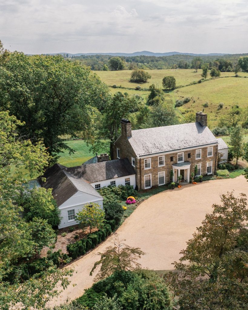 Aerial view of historic stone estate with white tent surrounded by rolling Virginia countryside and mountains