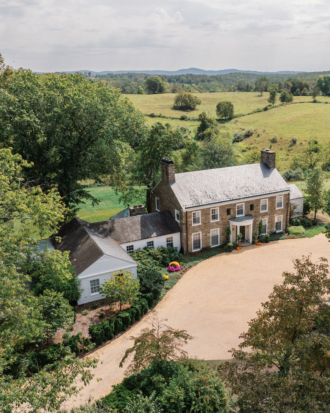 Aerial view of historic stone estate with white tent surrounded by rolling Virginia countryside and mountains