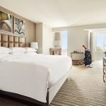 Spacious hotel room with king bed, tufted leather headboard, sitting area, and golf bag by the window