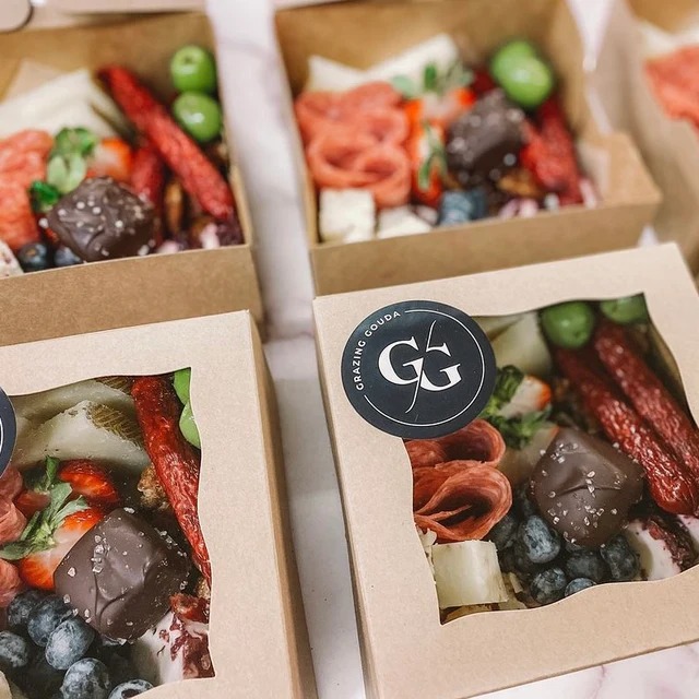 Grazing Gouda branded charcuterie boxes with meats, cheeses, chocolate, and fresh berries