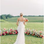 Bride in strapless gown holding colorful bouquet overlooking Virginia countryside with vibrant floral arrangements