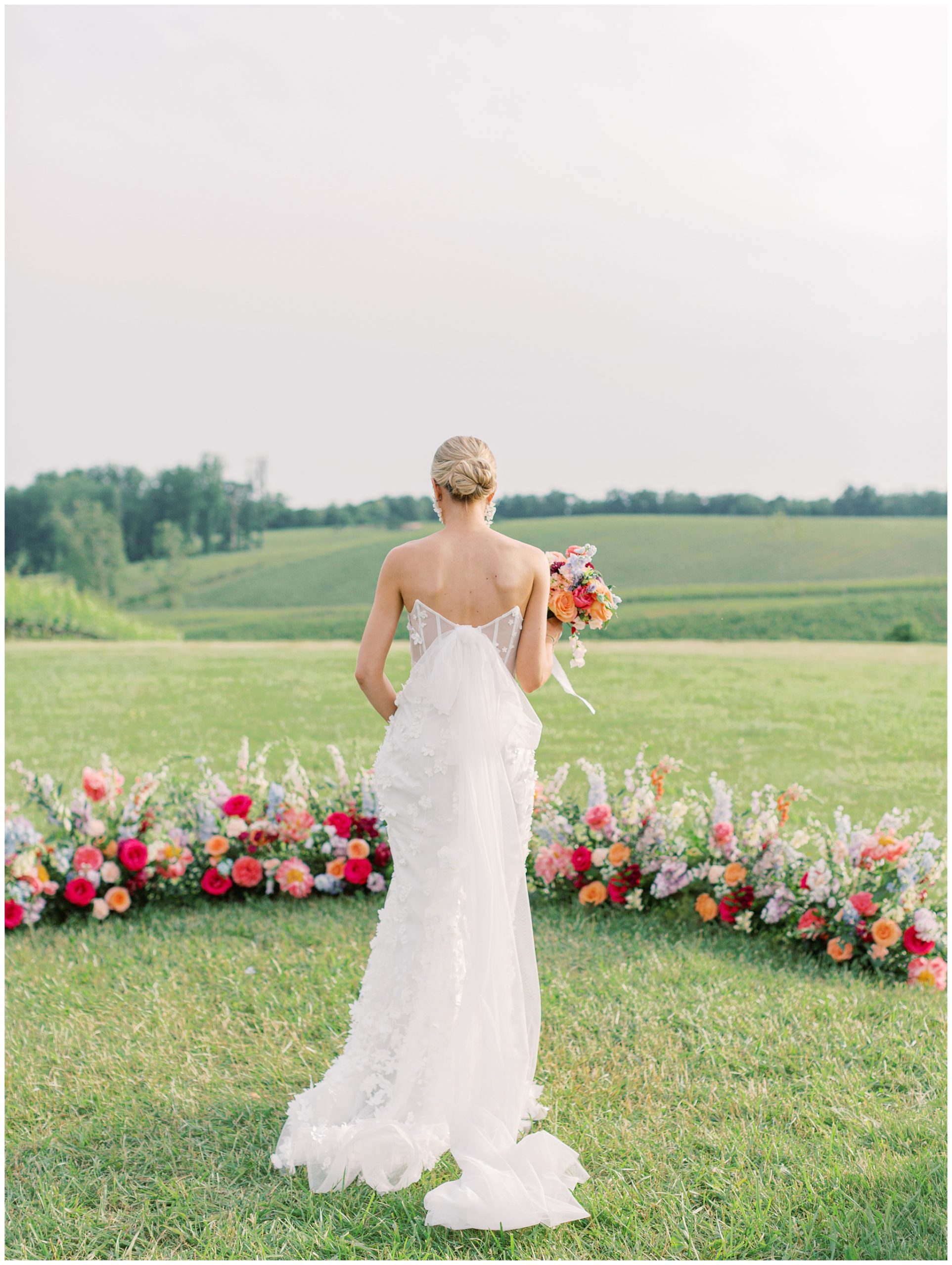 Bride in strapless gown holding colorful bouquet overlooking Virginia countryside with vibrant floral arrangements