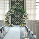 Modern wedding ceremony space with floral arch, white aisle runner, elegant seating, and candlelit walkway
