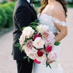 Bride and groom standing together, showcasing elegant bridal bouquet with roses, peonies, and greenery in pink and burgundy palette