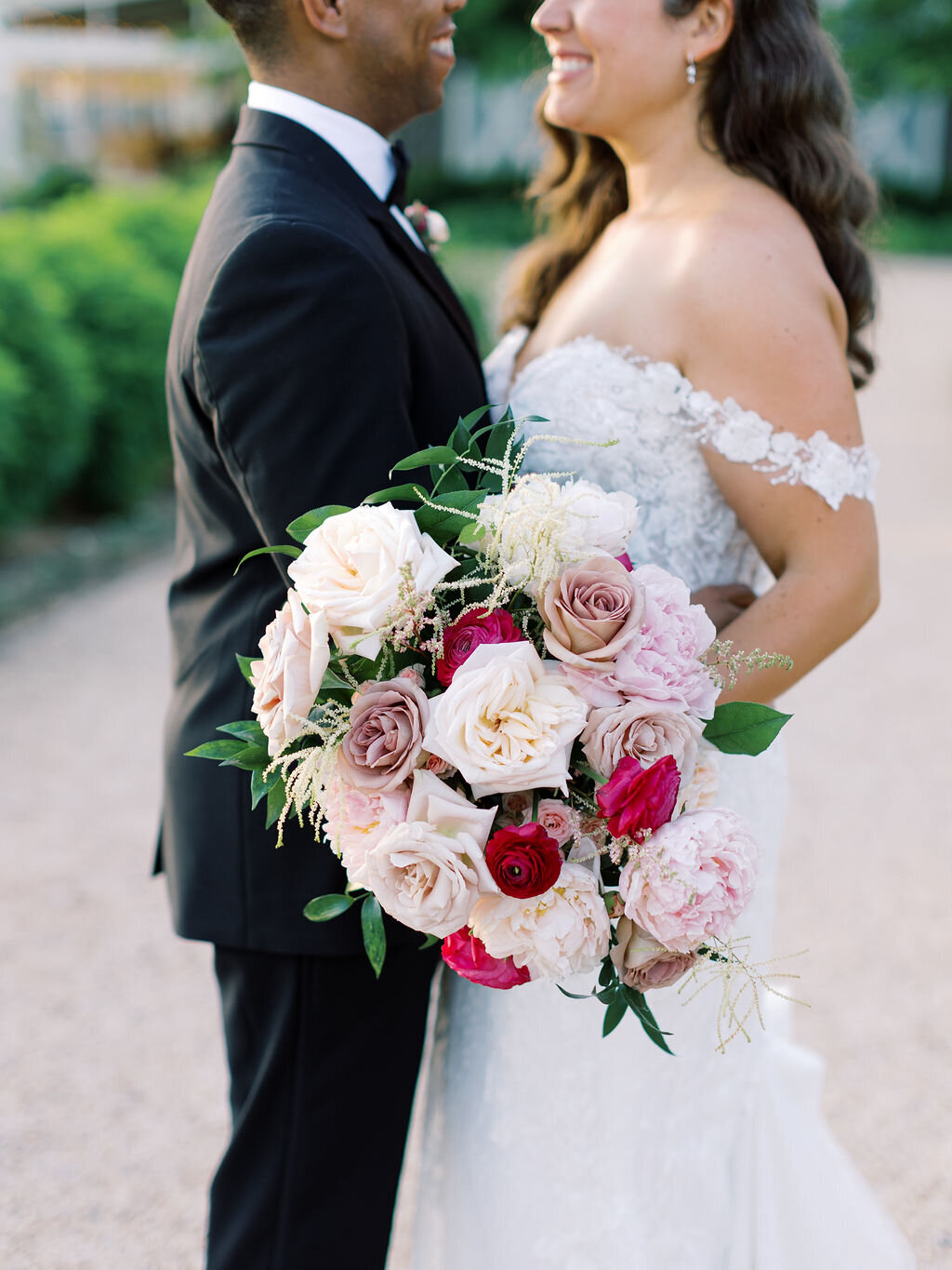 Bride and groom standing together, showcasing elegant bridal bouquet with roses, peonies, and greenery in pink and burgundy palette