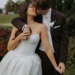 Newlyweds kissing, bride in strapless white gown and groom in dark suit with white boutonniere