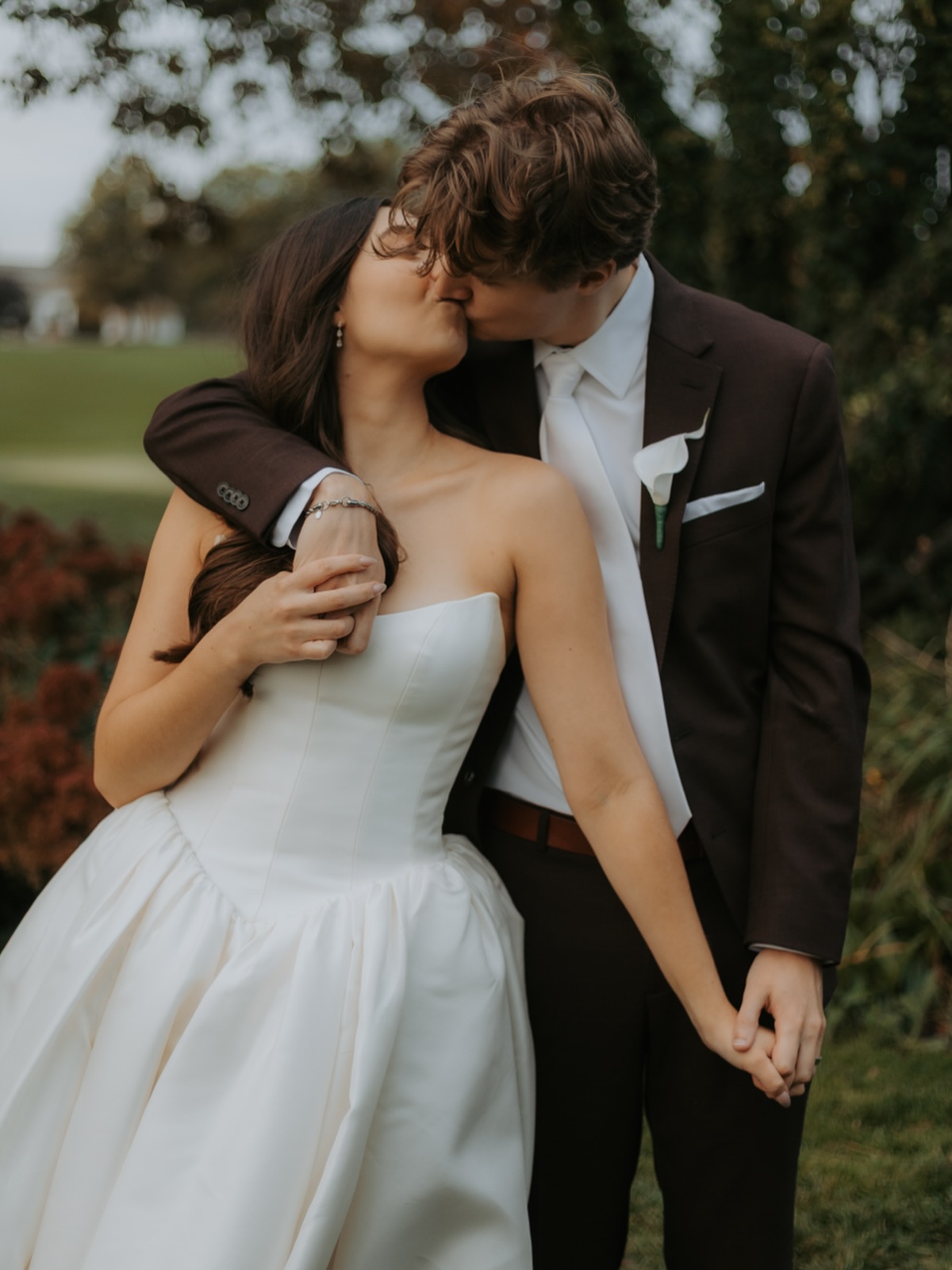 Newlyweds kissing, bride in strapless white gown and groom in dark suit with white boutonniere