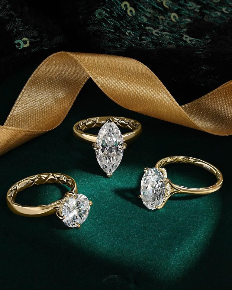 Three gold engagement rings with marquise, oval, and round diamonds featuring geometric textured bands on emerald velvet