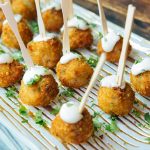 Golden-fried appetizer bites on wooden skewers with cream sauce and fresh herbs
