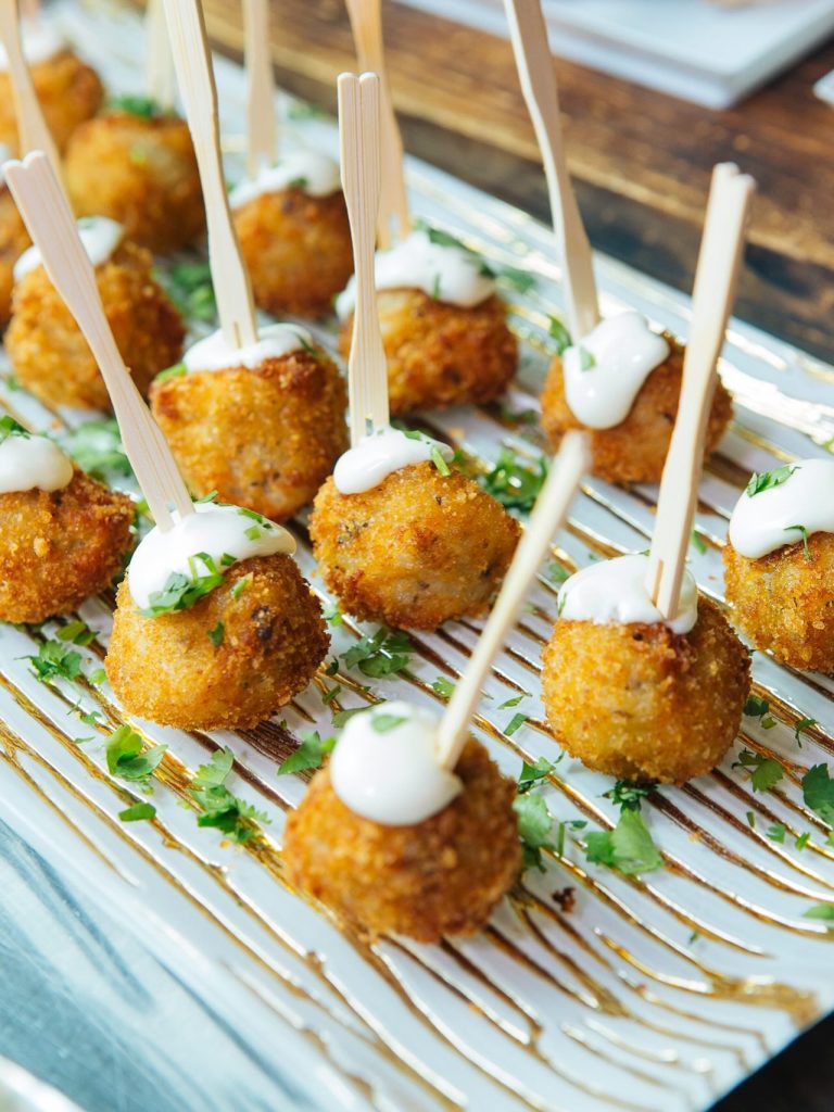 Golden-fried appetizer bites on wooden skewers with cream sauce and fresh herbs