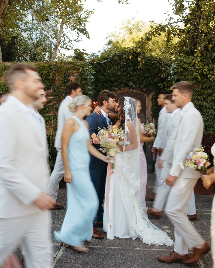 Garden wedding kiss captured with motion blur of guests and wedding party celebrating