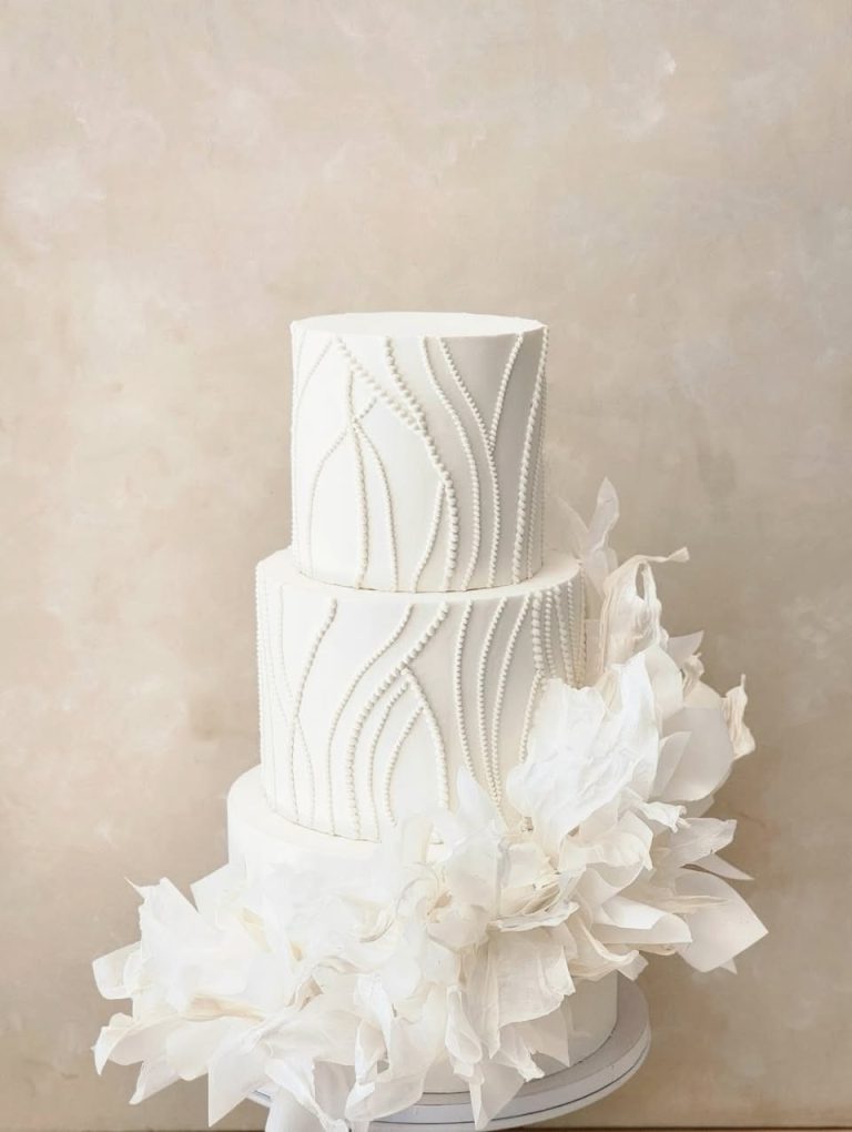 Three-tier white wedding cake with pearl beading and cascading white sugar flowers