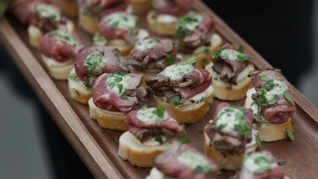 Elegant crostini appetizers with sliced beef, herb cream, and mushrooms arranged on a wooden serving board