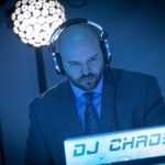 Wedding DJ in suit and headphones performing at event with illuminated DJ Chaos booth and disco ball