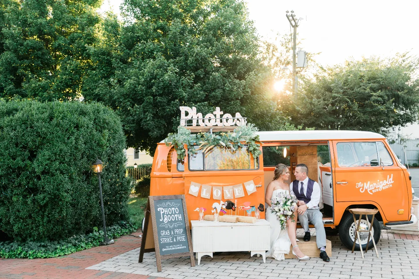 Bride and groom sitting in orange vintage VW van converted to photo booth at outdoor wedding reception