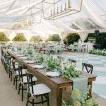 Elegant tented wedding reception with long farm tables, geometric gold chandeliers, and lush greenery centerpieces