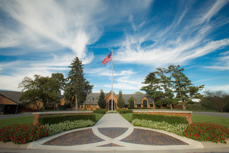 Nebraska country club wedding venue with brick entrance, landscaped gardens, American flag, and dramatic sky