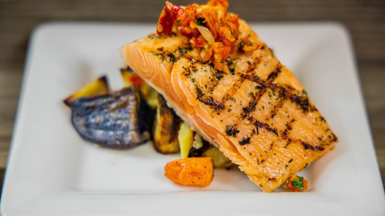 Herb-crusted grilled salmon fillet with roasted vegetables and lobster garnish on white plate