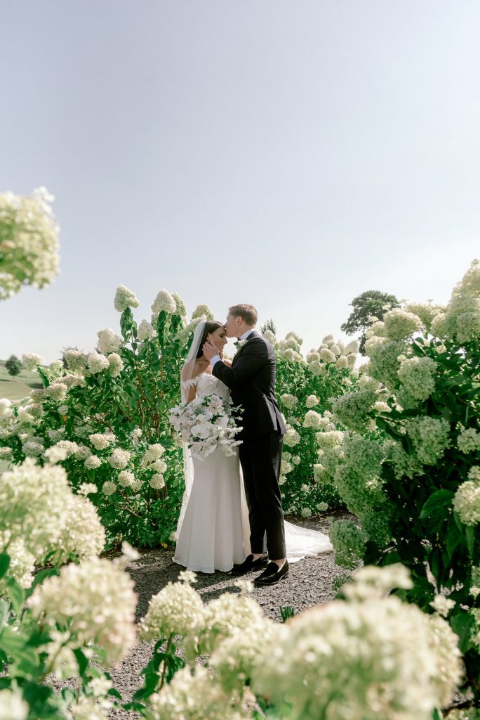 Wedding couple standing together in peaceful garden setting with white hydrangeas
