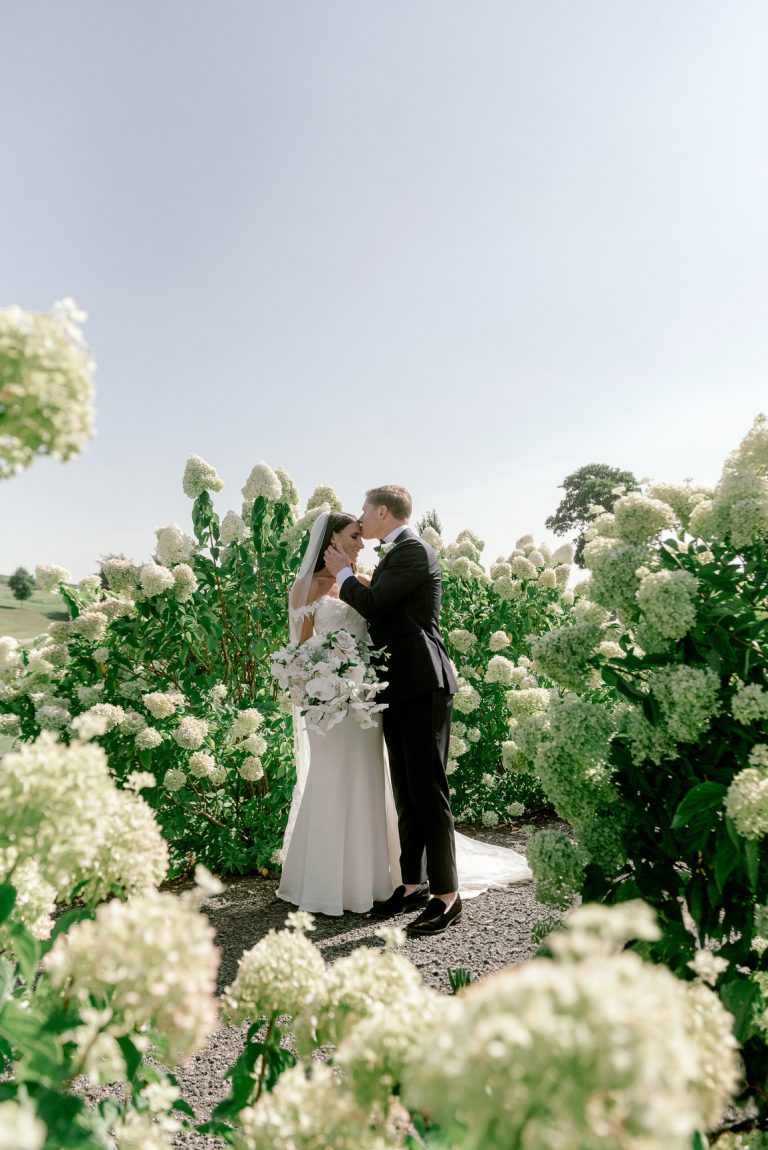 Wedding couple standing together in peaceful garden setting with white hydrangeas