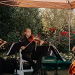 String trio with two violinists and cellist performing at outdoor garden ceremony