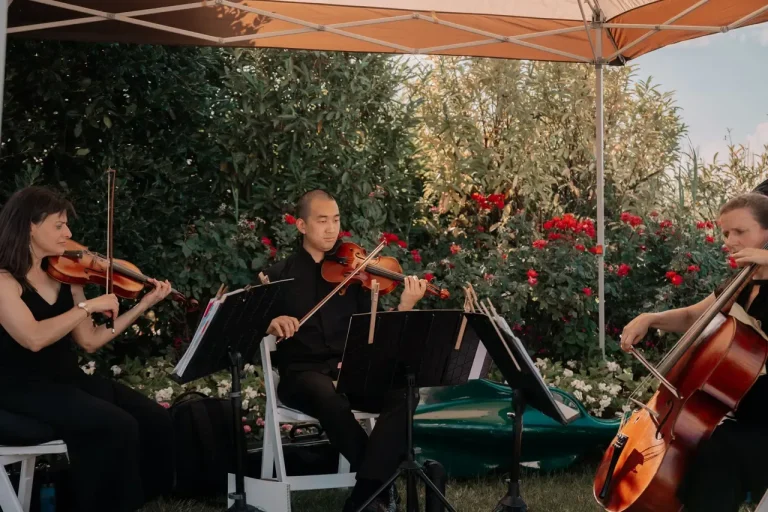 String trio with two violinists and cellist performing at outdoor garden ceremony