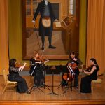 String quartet performing in formal hall beneath large historical portrait of man in Masonic apron