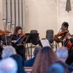 String quartet performing for seated audience in concert hall with organ pipes visible