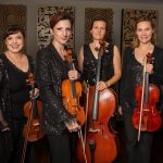 Four female musicians in black evening wear posing with violins and cello against decorative panel backdrop