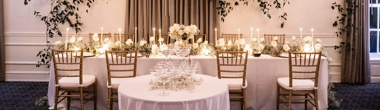 Tiered champagne glass tower with white roses and candles on reception table