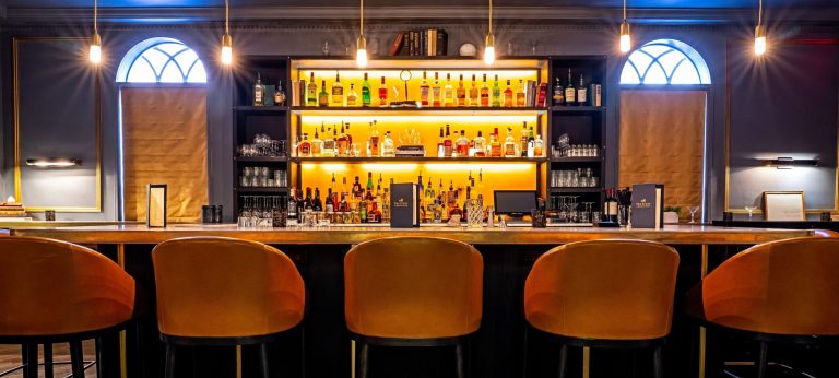 Sophisticated bar with backlit shelves of spirits, pendant lighting, and orange velvet seating