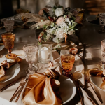 Elegant wedding table setting with golden silk napkins, vintage amber glassware, floral centerpiece, and copper flatware