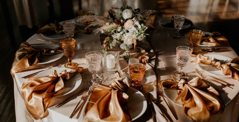 Elegant wedding table setting with golden silk napkins, vintage amber glassware, floral centerpiece, and copper flatware