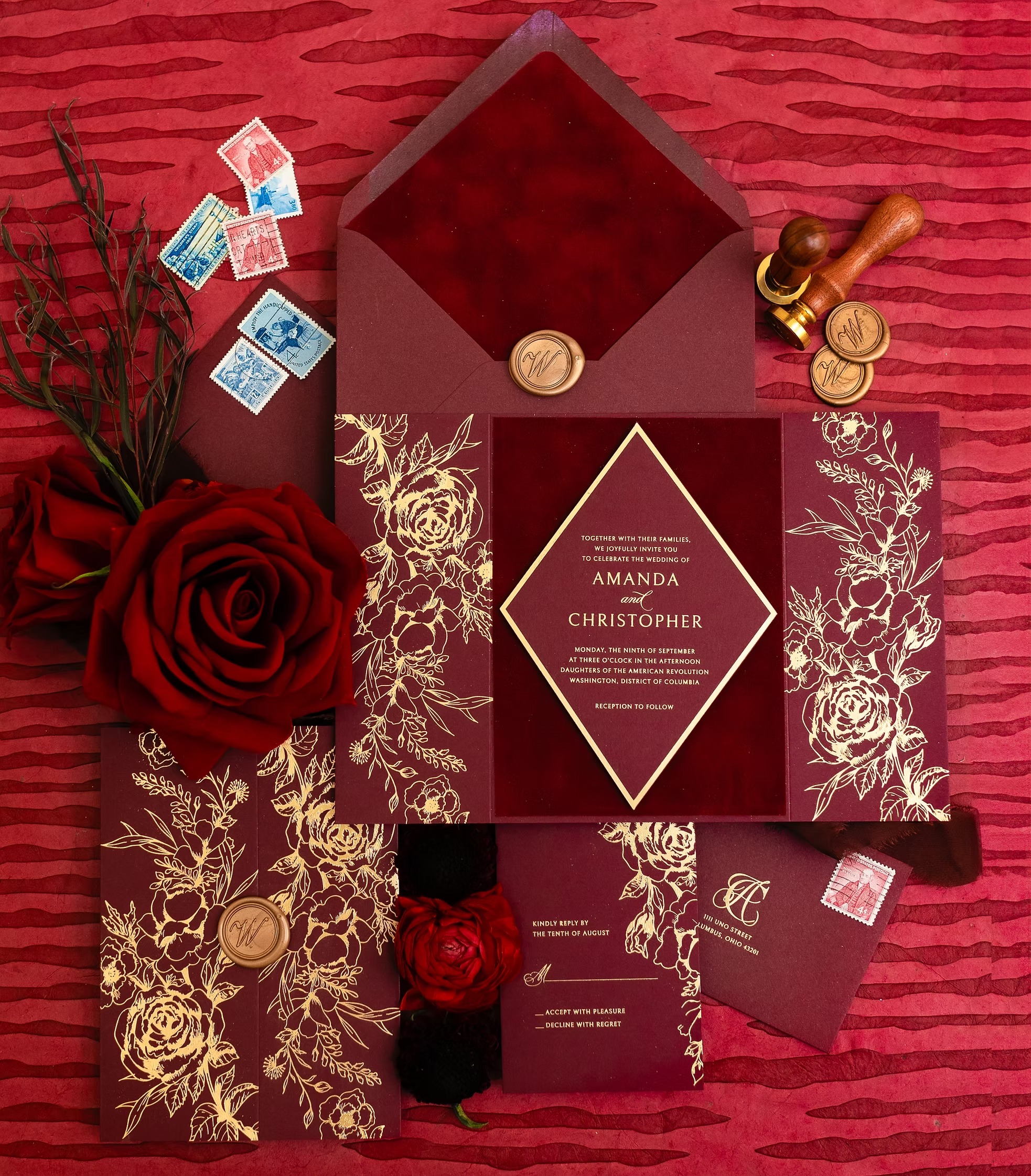 Burgundy wedding invitation suite with gold foil floral design, wax seals, vintage stamps, and red roses