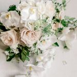 Wedding bouquet with white orchids, blush garden roses, and trailing greenery photographed from above