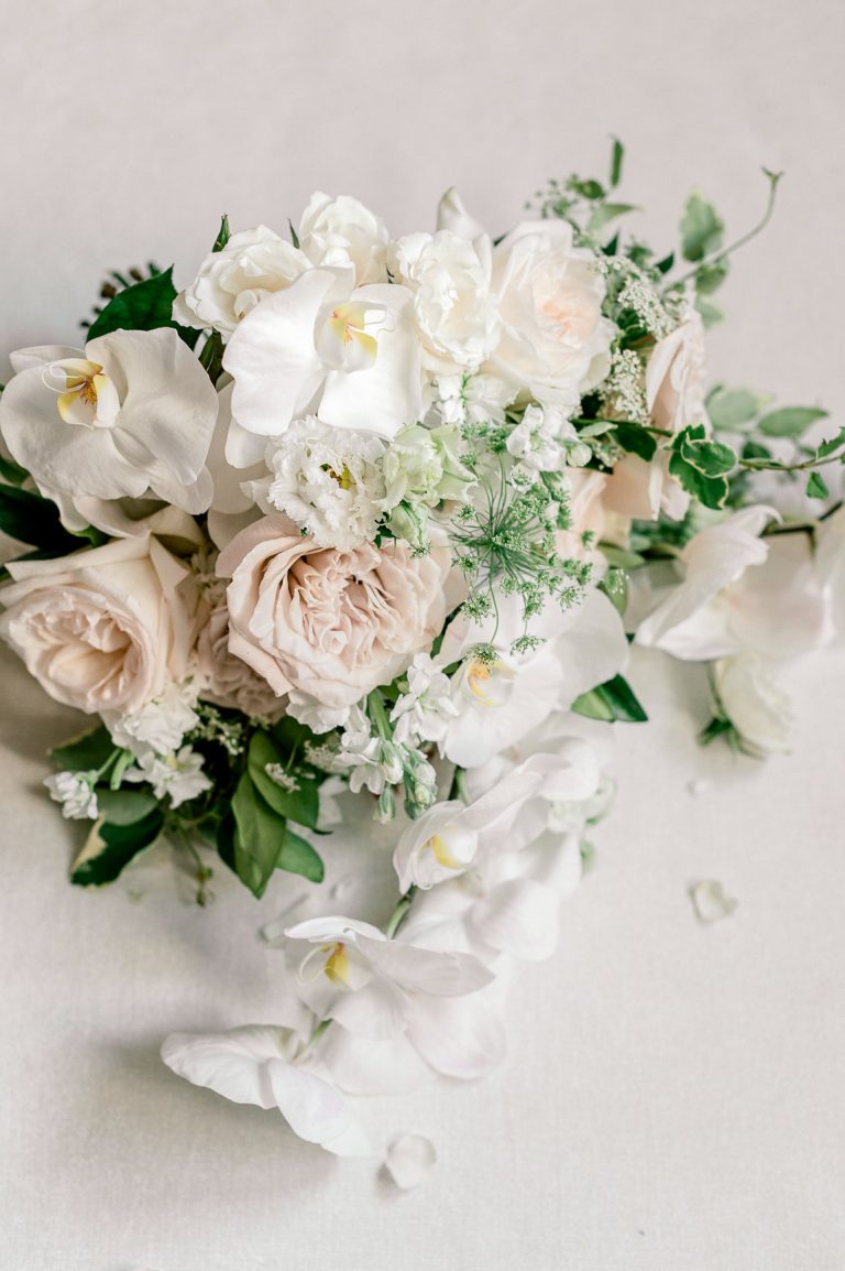 Wedding bouquet with white orchids, blush garden roses, and trailing greenery photographed from above