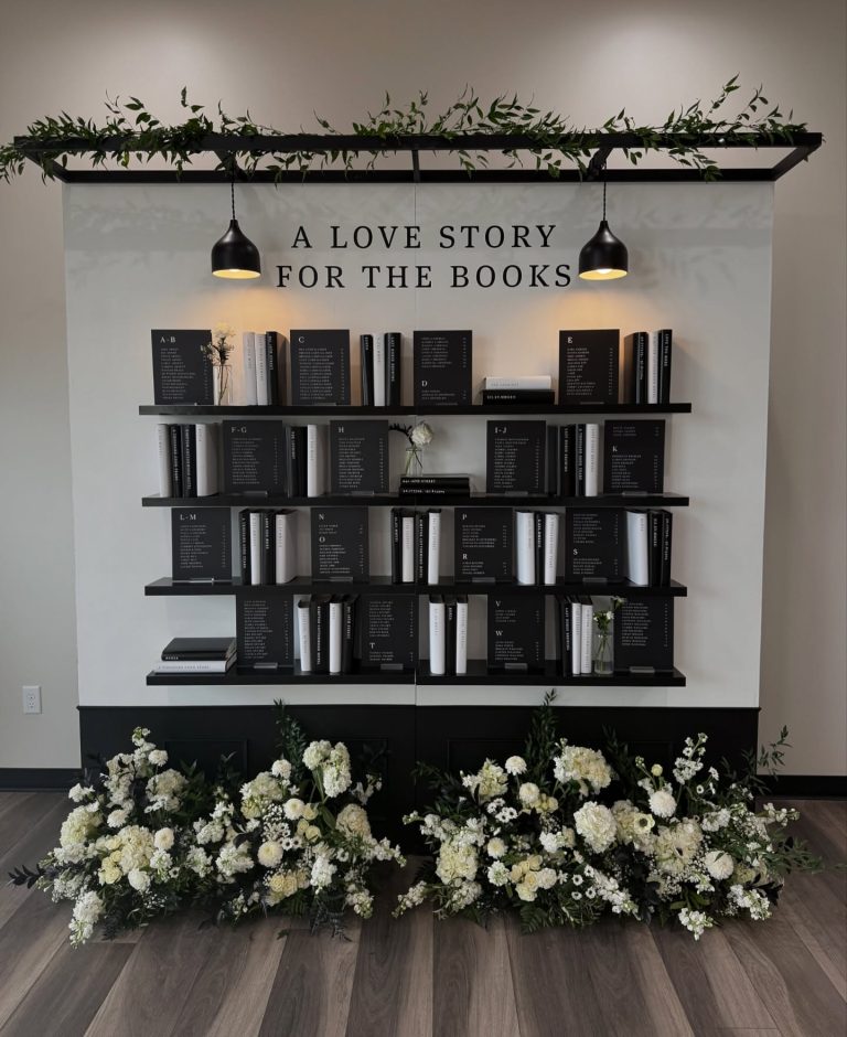 Modern wedding seating chart styled as bookshelf with "A Love Story for the Books" sign, featuring white floral arrangement at base